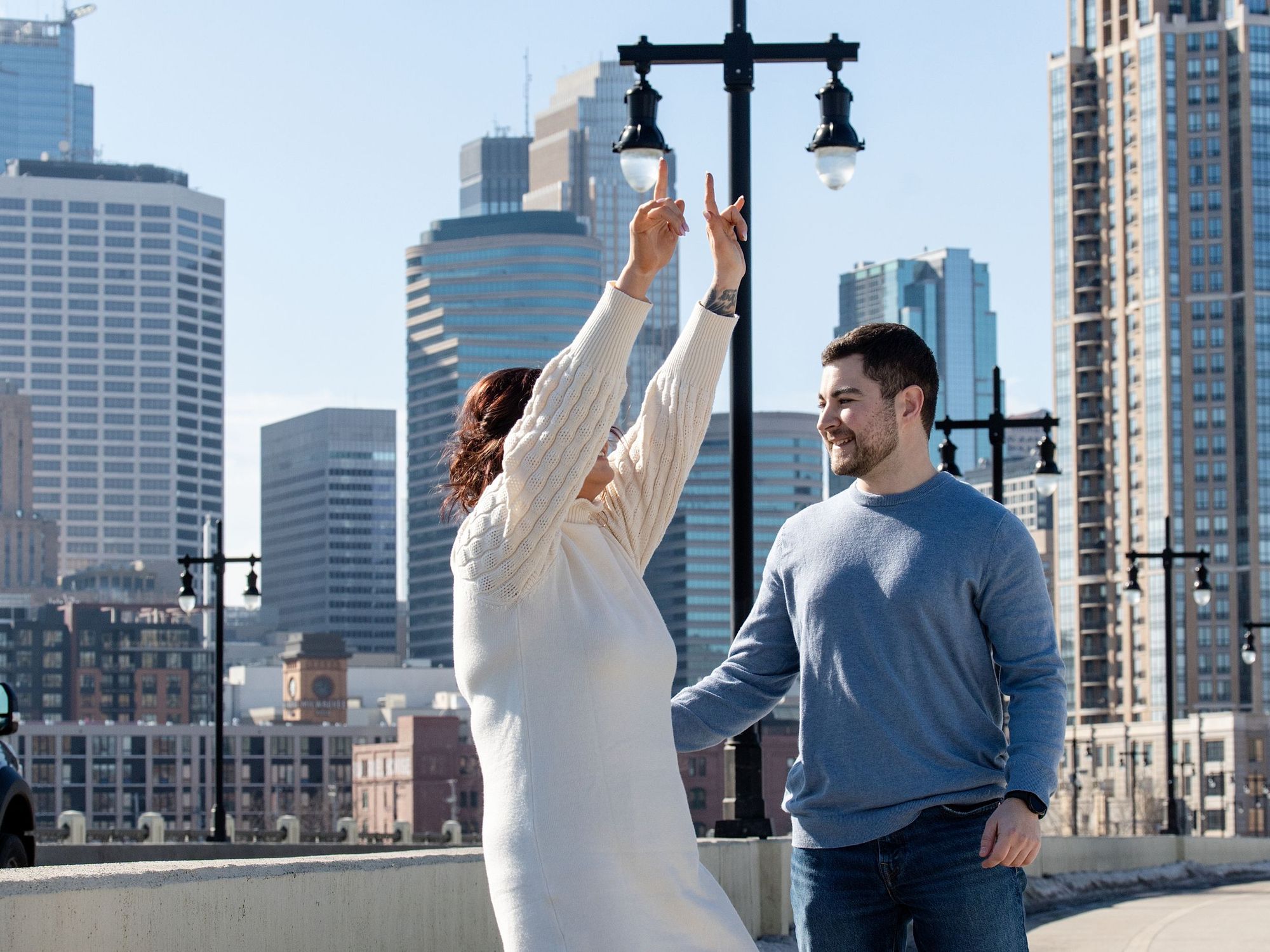 She said yes: a woman celebrates with arms raised on a bridge with the Minneapolis skyline behind