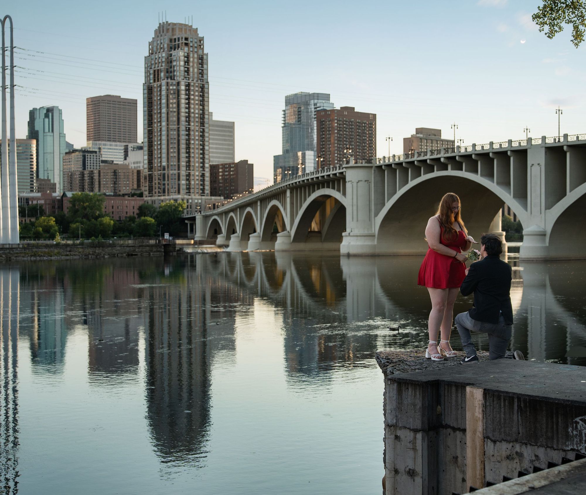 A proposal on the Minneapolis riverfront at dusk, the skyline and bridge reflected in the river