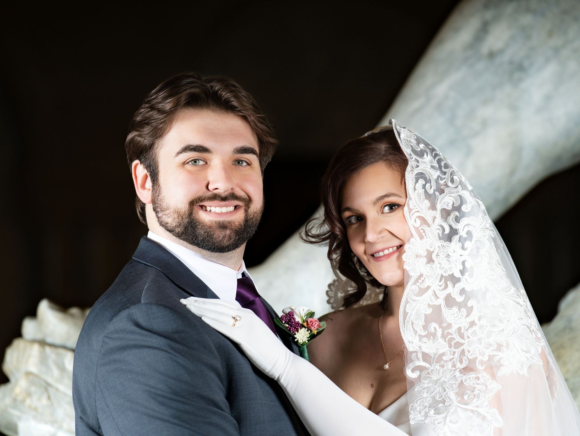 Bride and groom smiling beside a marble sculpture